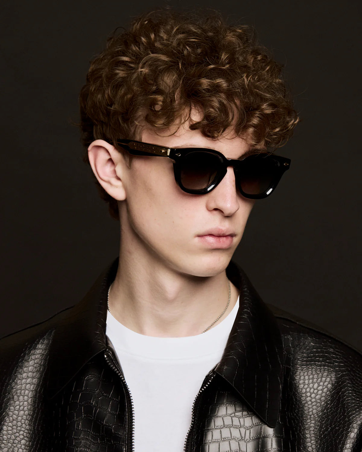 Person wearing sunglasses and a black leather jacket against a dark background